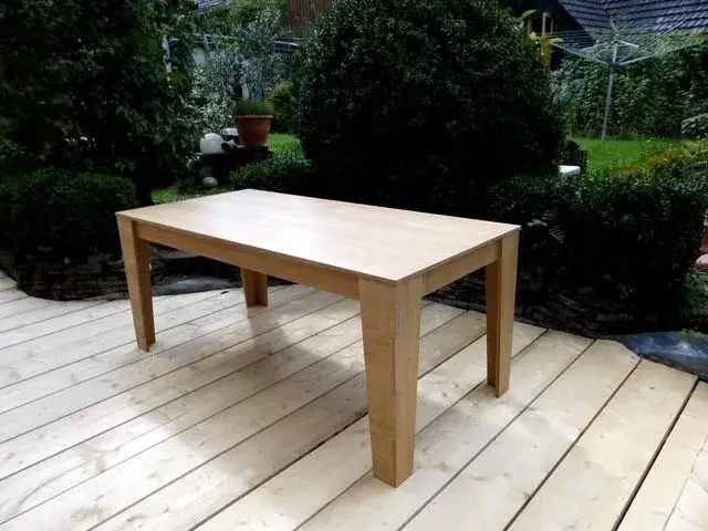 Rechteckiger Holztisch steht auf einer hellen Terrasse im Garten.