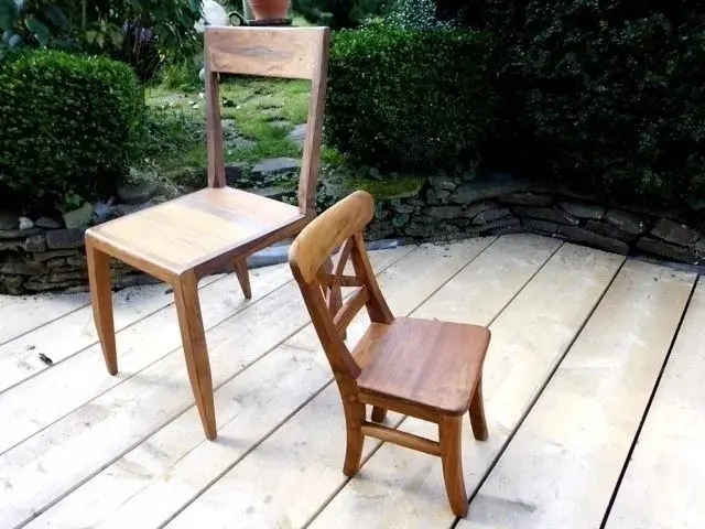 Zwei unterschiedlich große Holzstühle stehen auf einer Terrasse im Garten.