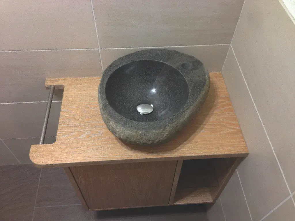 Schwarzes Steinauswaschbecken auf einem Holzunterschrank im Badezimmer.