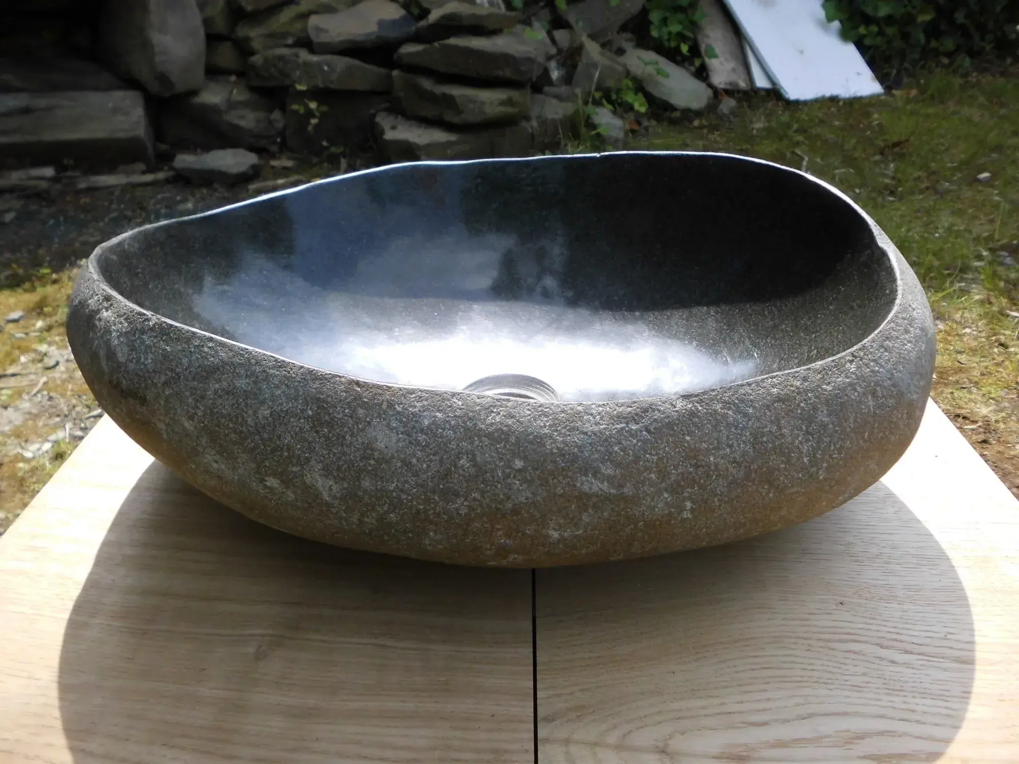 Großes, ovales Waschbecken aus Stein auf einem Holztisch im Freien
